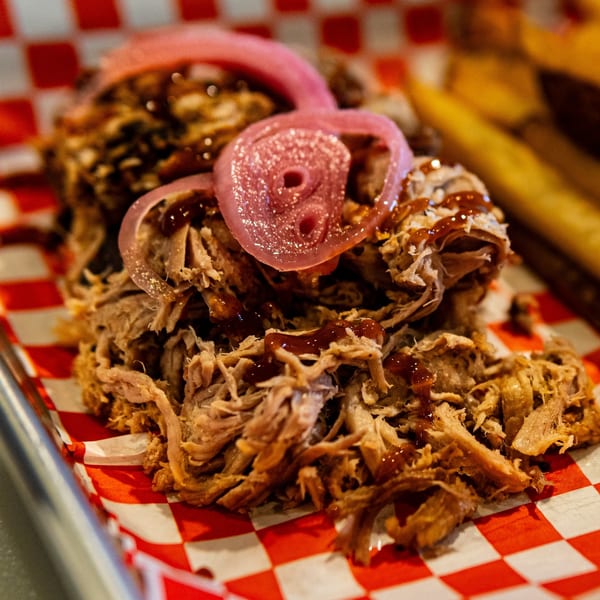 Close-up of Blind Raven BBQ's pulled pork with pickled red onions and barbecue sauce on checkered paper.