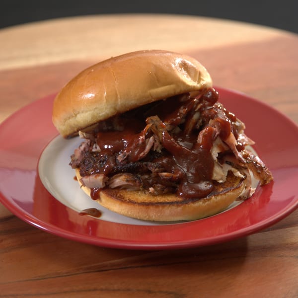 A Blind Raven BBQ pulled pork sandwich, generously topped with barbecue sauce, on a red plate.