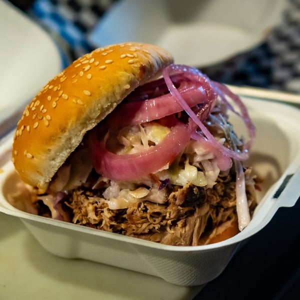 Close-up of a Blind Raven BBQ pulled pork sandwich with coleslaw and pickled red onions.