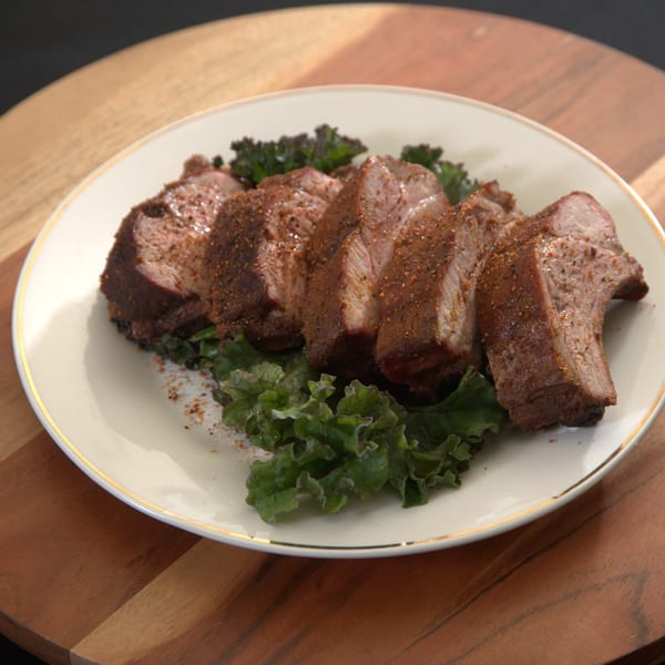 Slices of seasoned, smoked BBQ meat on a bed of green kale, served on a white plate.