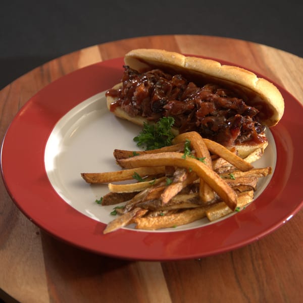 Blind Raven BBQ's pulled pork sandwich with BBQ sauce and caramelized onions, served with fries.