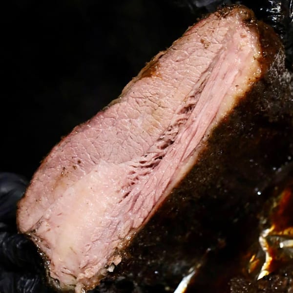 Close-up of a thick slice of Blind Raven BBQ brisket, showing its pink interior and dark, smoky crust.